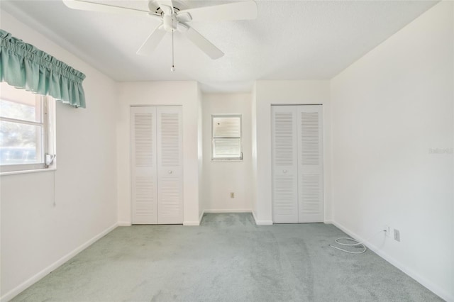 unfurnished bedroom featuring ceiling fan, light carpet, and multiple closets