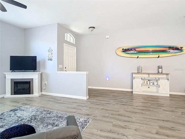 living room with ceiling fan, a fireplace, baseboards, and wood finished floors