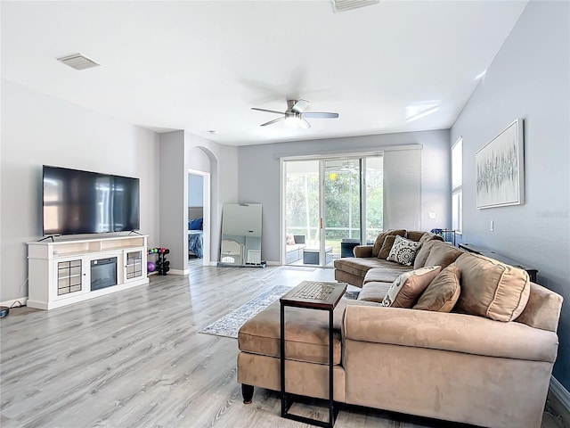 living area with baseboards, visible vents, arched walkways, a glass covered fireplace, and light wood-type flooring