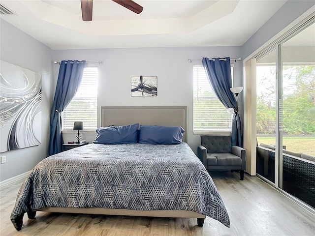 bedroom featuring visible vents, wood finished floors, a raised ceiling, a ceiling fan, and access to outside