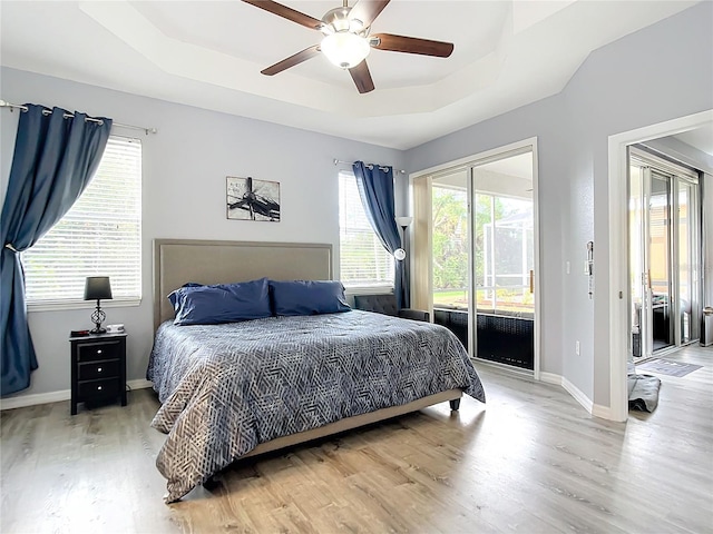 bedroom featuring a raised ceiling, a ceiling fan, wood finished floors, baseboards, and access to exterior