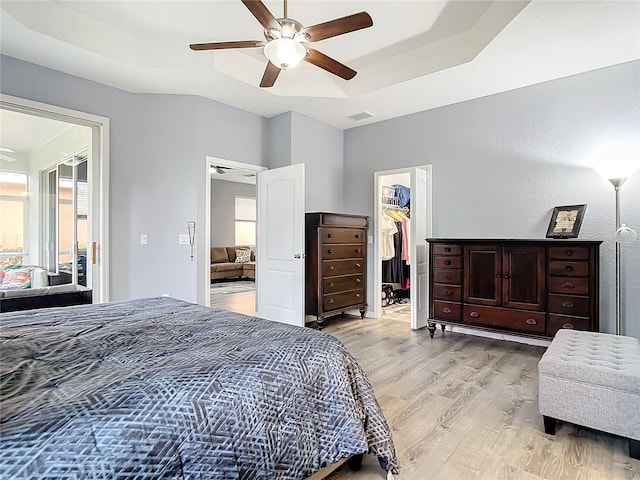 bedroom featuring light wood-type flooring, a raised ceiling, visible vents, and a walk in closet