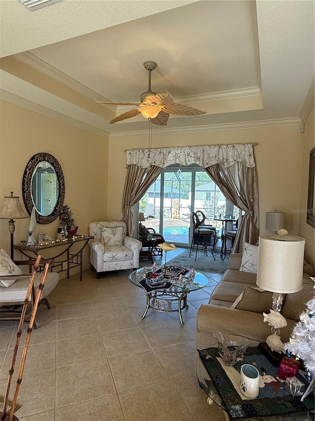 living room featuring a raised ceiling, ceiling fan, tile patterned floors, and ornamental molding