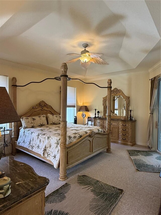 bedroom featuring ceiling fan, carpet floors, ornamental molding, and a tray ceiling