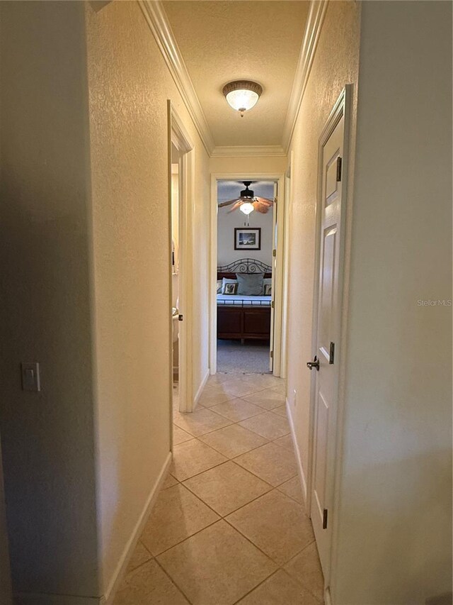 hallway featuring light tile patterned flooring, ornamental molding, and a textured ceiling