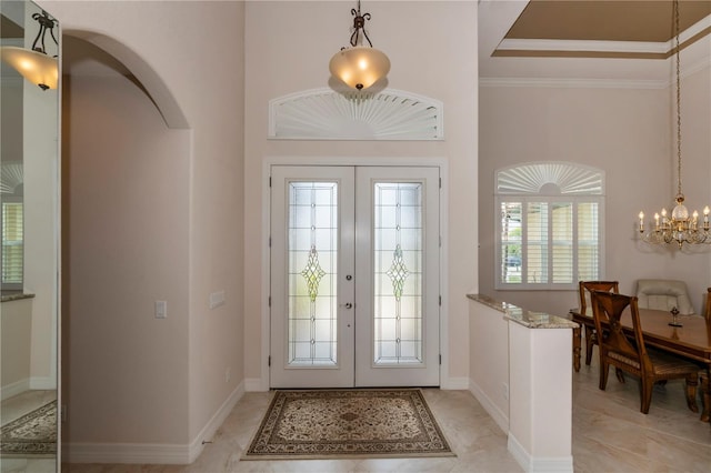 foyer entrance with french doors, a towering ceiling, a chandelier, and ornamental molding