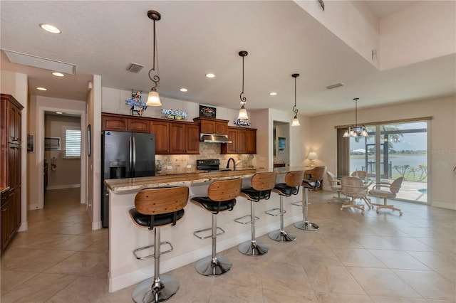 kitchen with decorative backsplash, stainless steel fridge, light stone countertops, a breakfast bar, and black electric range