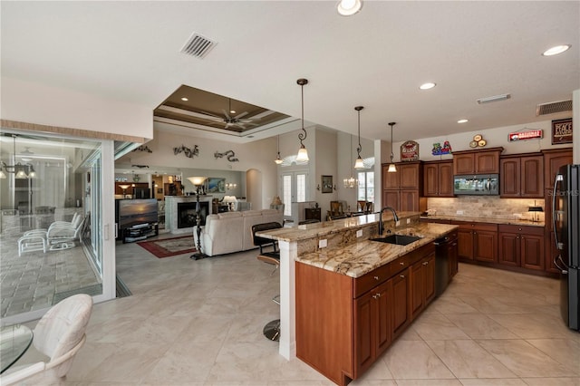 kitchen featuring a large island with sink, ceiling fan with notable chandelier, hanging light fixtures, sink, and tasteful backsplash