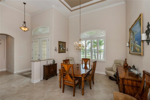 dining room with a notable chandelier, ornamental molding, a towering ceiling, and french doors