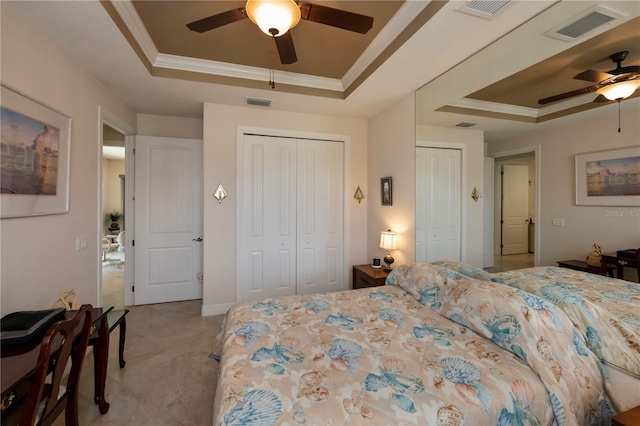 bedroom featuring ceiling fan, two closets, ornamental molding, and a tray ceiling