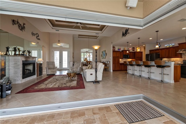 tiled living room featuring ceiling fan, a tray ceiling, a high ceiling, and french doors