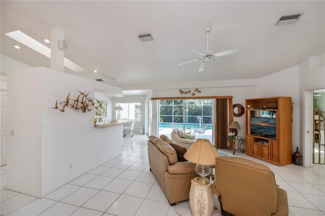 living room featuring ceiling fan, vaulted ceiling with skylight, and light tile patterned floors