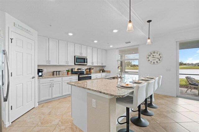 kitchen with light stone countertops, stainless steel appliances, sink, white cabinetry, and an island with sink