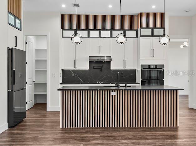 kitchen with white cabinets, black fridge, sink, hanging light fixtures, and an island with sink