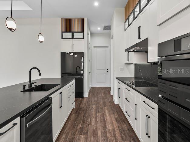 kitchen with dark wood-type flooring, black appliances, sink, hanging light fixtures, and white cabinetry