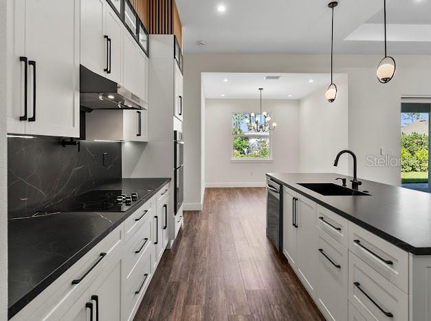 kitchen with pendant lighting, white cabinetry, sink, and a kitchen island with sink