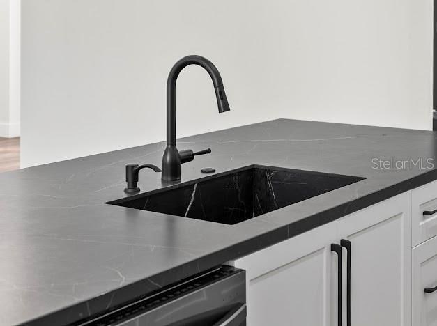 room details with white cabinets, stainless steel dishwasher, and sink