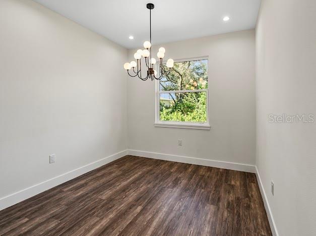 empty room with a notable chandelier and dark hardwood / wood-style flooring