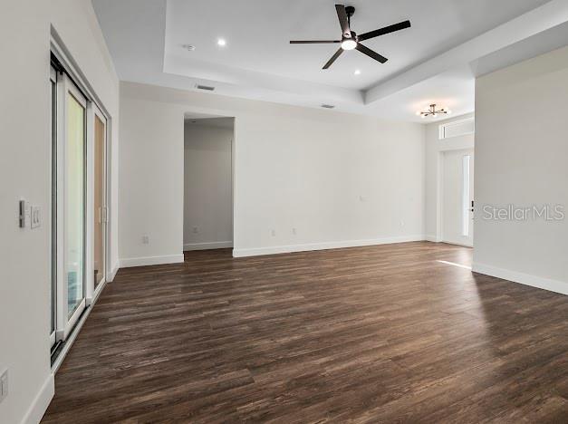 empty room with dark hardwood / wood-style floors, ceiling fan, and a raised ceiling