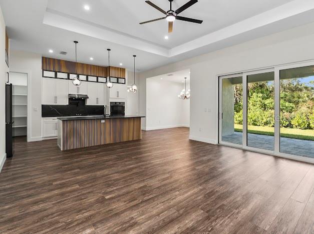 kitchen with decorative light fixtures, a tray ceiling, a center island with sink, white cabinets, and black appliances