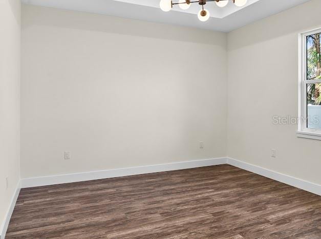 unfurnished room with a chandelier and dark wood-type flooring