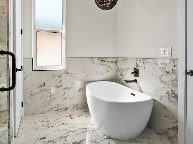 bathroom featuring a wealth of natural light, plus walk in shower, and tile walls