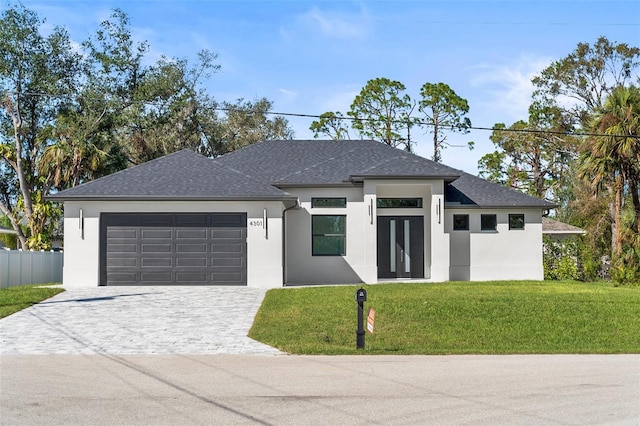prairie-style house with decorative driveway, a front lawn, a shingled roof, an attached garage, and stucco siding