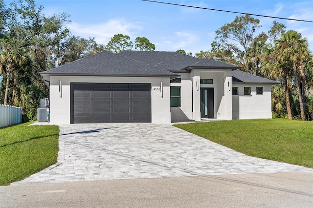 prairie-style home featuring cooling unit, decorative driveway, stucco siding, a front lawn, and a garage