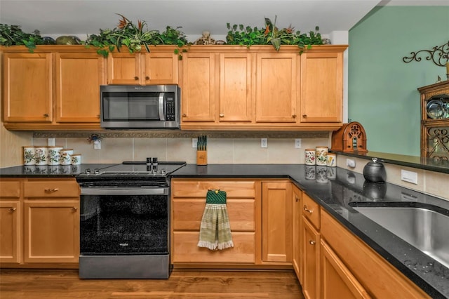 kitchen with appliances with stainless steel finishes, tasteful backsplash, light hardwood / wood-style flooring, and dark stone counters