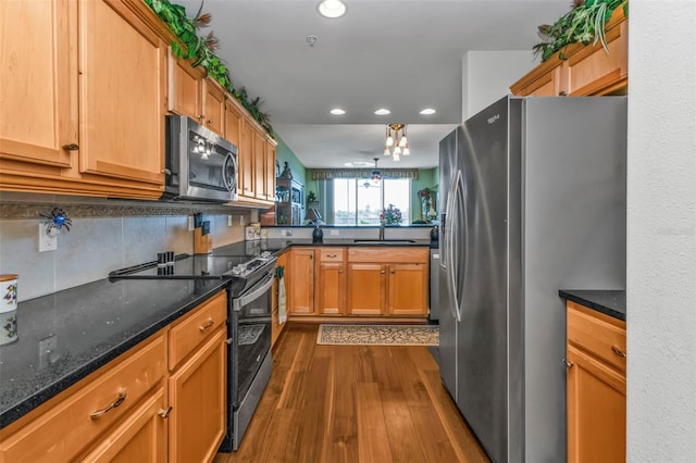 kitchen with sink, tasteful backsplash, dark hardwood / wood-style flooring, dark stone counters, and appliances with stainless steel finishes