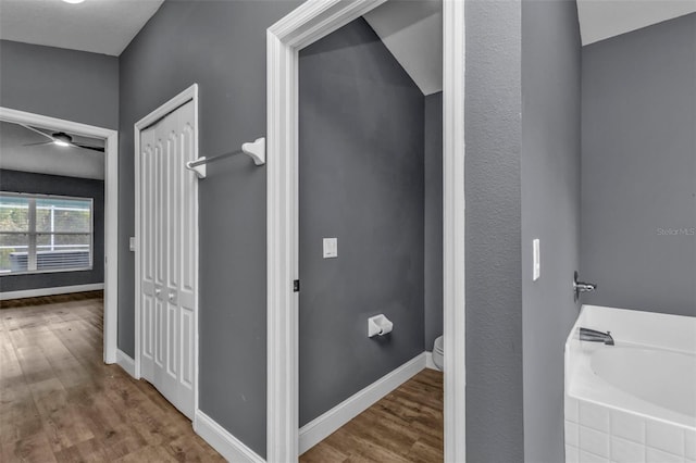 bathroom featuring a relaxing tiled tub, hardwood / wood-style floors, and toilet