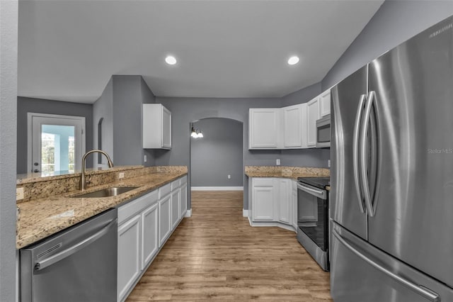 kitchen featuring sink, appliances with stainless steel finishes, light stone countertops, white cabinets, and light wood-type flooring