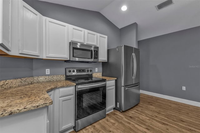 kitchen featuring lofted ceiling, white cabinetry, light stone counters, light wood-type flooring, and appliances with stainless steel finishes