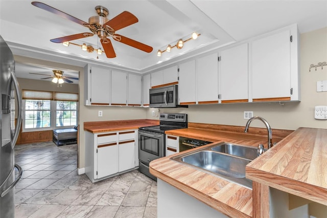 kitchen with wooden counters, appliances with stainless steel finishes, ceiling fan, sink, and white cabinets