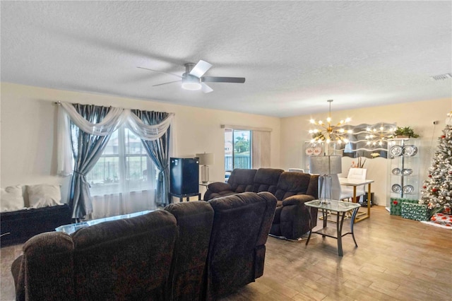 living room featuring ceiling fan with notable chandelier, light hardwood / wood-style floors, and a textured ceiling