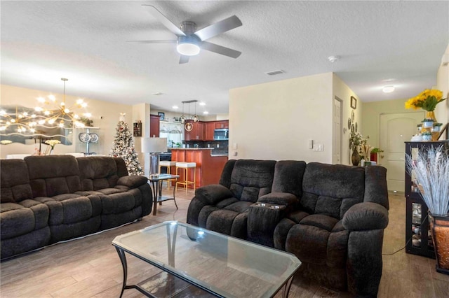 living room featuring a textured ceiling, ceiling fan with notable chandelier, and light wood-type flooring