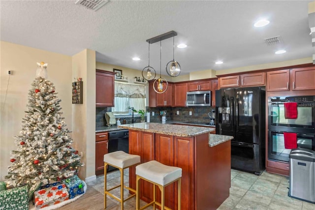 kitchen featuring light stone countertops, backsplash, black appliances, decorative light fixtures, and a kitchen island