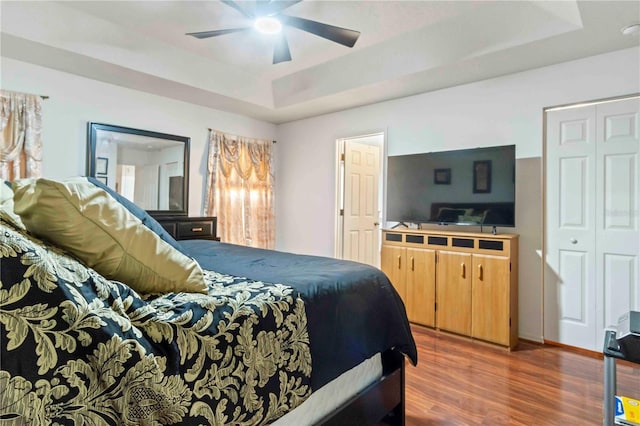 bedroom featuring a raised ceiling, ceiling fan, a closet, and dark wood-type flooring