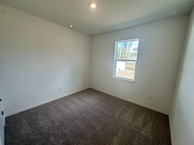 spare room with dark carpet, a textured ceiling, and baseboards