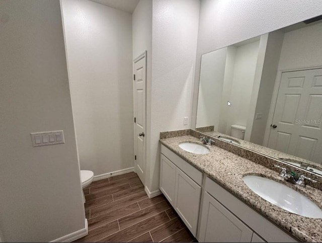 bathroom featuring toilet, baseboards, a sink, and wood finish floors