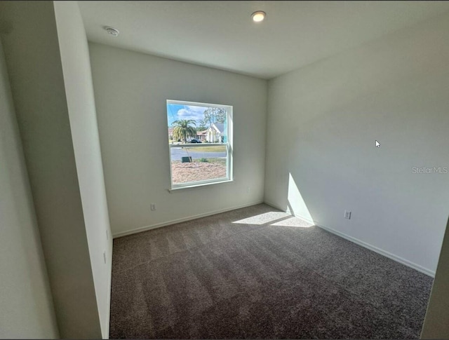 spare room with dark carpet and baseboards