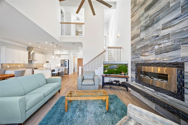 living room with a tile fireplace, a high ceiling, sink, crown molding, and light wood-type flooring