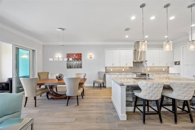 kitchen featuring white cabinets, pendant lighting, light stone counters, and wall chimney range hood