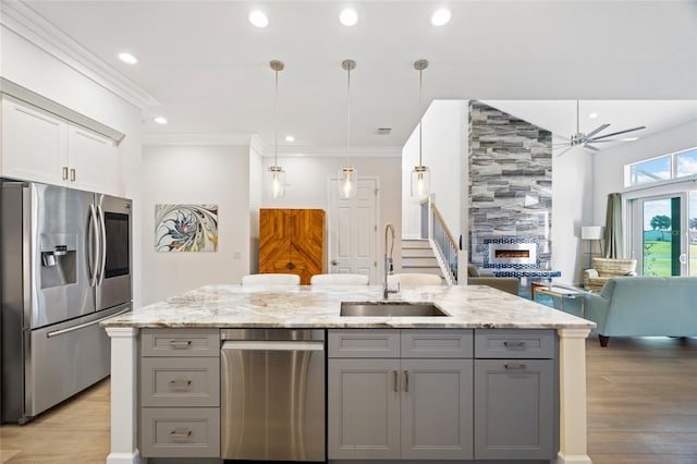 kitchen with stainless steel appliances, a tiled fireplace, gray cabinetry, and sink