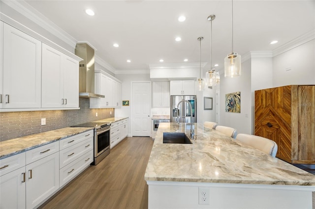 kitchen featuring white cabinetry, wall chimney exhaust hood, stainless steel appliances, a large island with sink, and hardwood / wood-style floors