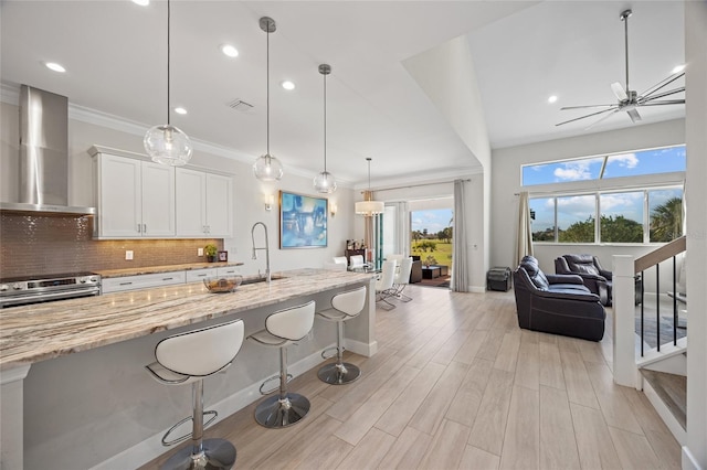 kitchen featuring sink, wall chimney exhaust hood, light stone countertops, stainless steel range, and white cabinetry