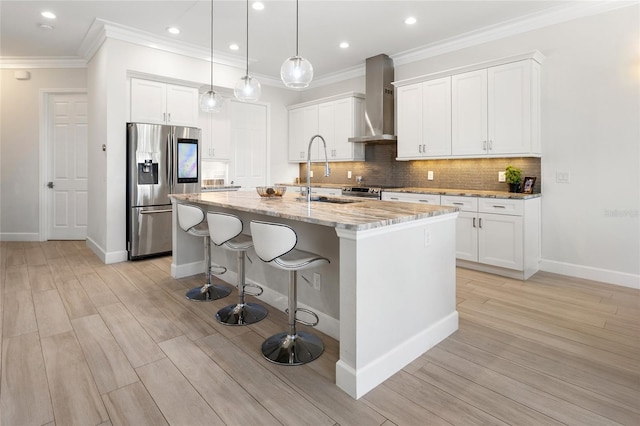 kitchen with appliances with stainless steel finishes, wall chimney exhaust hood, sink, a center island with sink, and white cabinetry