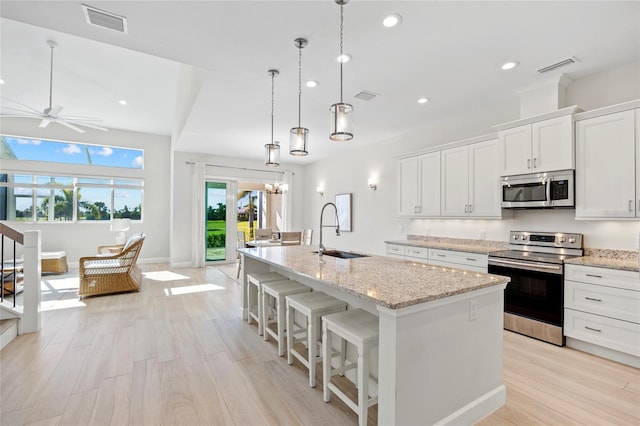 kitchen featuring white cabinetry, sink, stainless steel appliances, pendant lighting, and a center island with sink