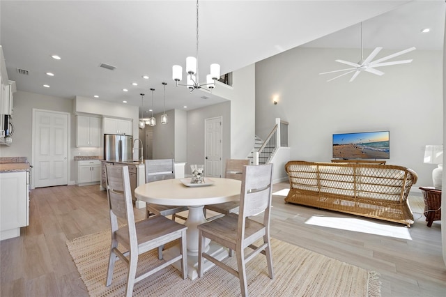 dining room featuring ceiling fan with notable chandelier, light hardwood / wood-style floors, high vaulted ceiling, and sink