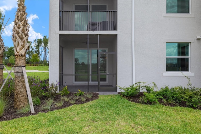 view of exterior entry featuring a lawn and stucco siding